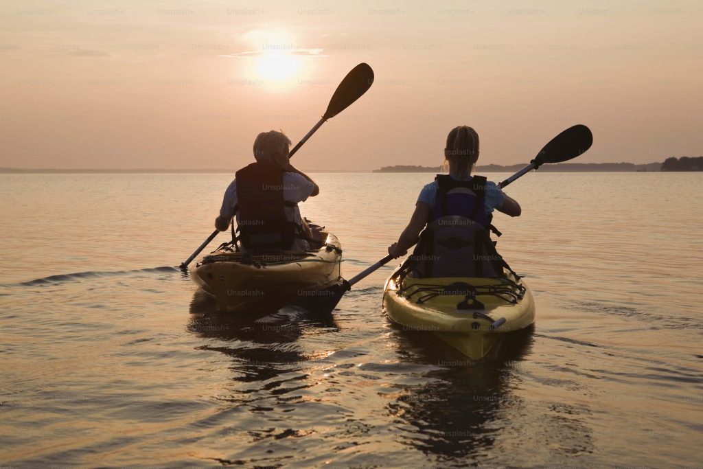 Couple kayaking on calm Maui ocean water at golden hour sunset